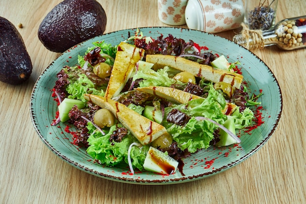 Leckerer Salat mit Tofu, Avocado und Olivensalat in einer weißen Schüssel auf einem Holztisch. Vegetarisches Essen. Leckeres und gesundes Essen