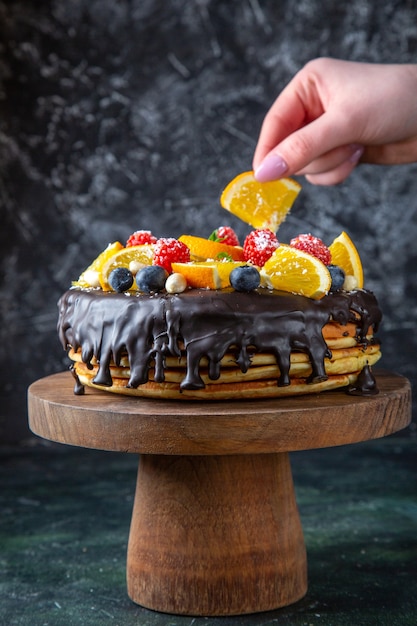 Leckerer Schokoladenkuchen der Vorderansicht mit frischen Früchten auf dunkler Wand