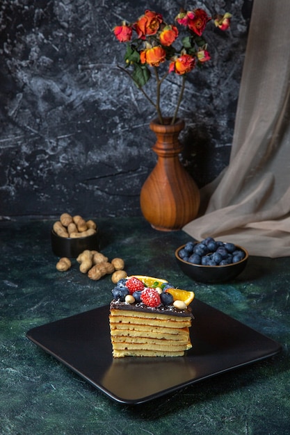 Leckerer Schokoladenkuchen der Vorderansicht mit Früchten auf dunkler Wand