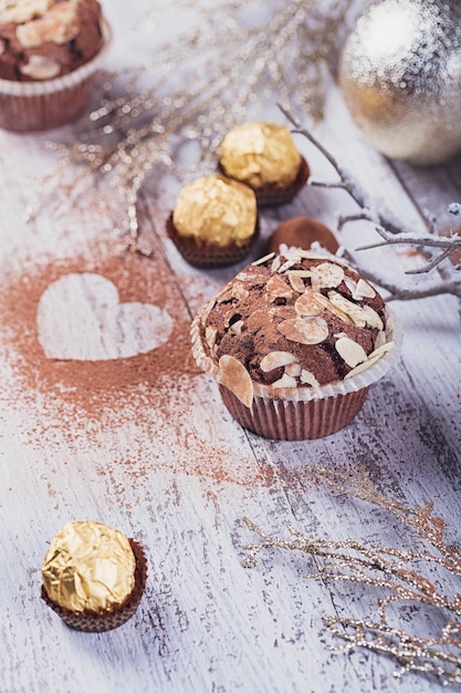 Leckerer Schokoladenkuchen mit Süßigkeiten, herzförmigem Kakaopulver und Winterdekoration auf weißem rustikalem Holztisch. Winterurlaub Hintergrund.