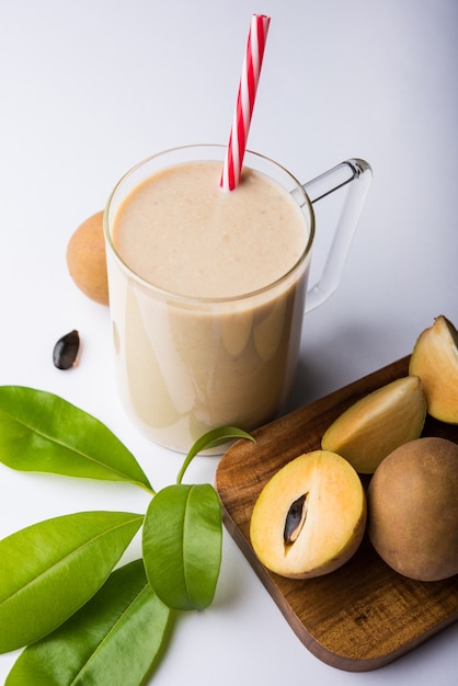 Leckerer und gesunder Chickoo, Chikoo ODER Sapota Milkshake. Es ist eine gesunde Frucht, die mit Milch und Eis gemischt wird und in einem Glas auf buntem oder hölzernem Hintergrund serviert wird. Selektiver Fokus