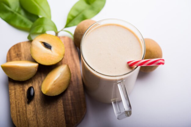 Leckerer und gesunder Chickoo, Chikoo ODER Sapota Milkshake. Es ist eine gesunde Frucht, die mit Milch und Eis gemischt wird und in einem Glas auf buntem oder hölzernem Hintergrund serviert wird. Selektiver Fokus