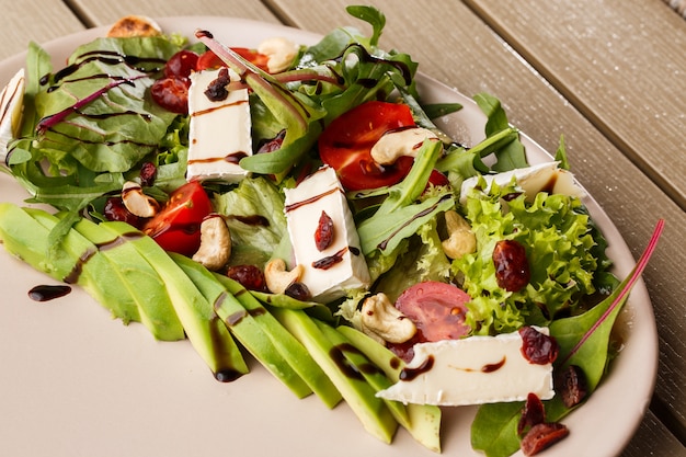 Leckerer und gesunder Salat mit Rucola, Brie, Käse, Avocado, Kirschtomaten, trockenen Preiselbeeren und Cashewnüssen.