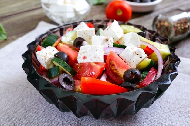 Leckerer Vitaminsalat mit frischem Gemüse, Ziegenkäse, schwarzen Oliven, Basilikumsauce auf einem weißen Teller auf einem Holztisch.