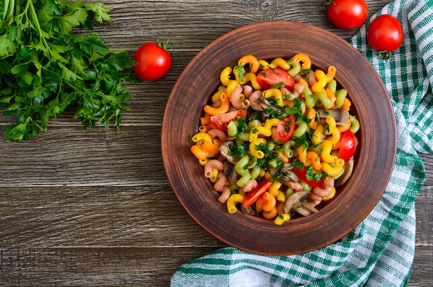 Leckerer warmer Salat. Farbige Nudeln mit Pilzen und frischen Tomaten in einer Schüssel auf einem Holztisch. Pasta colorata. Die Draufsicht