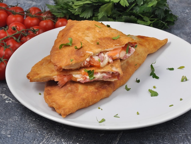 Leckeres Cheburek mit Tomaten und Käse und Kräutern auf einem weißen Teller