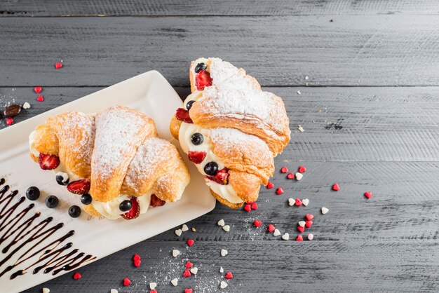 Foto leckeres croissant mit früchten und tasse kaffee auf dem holzhintergrund