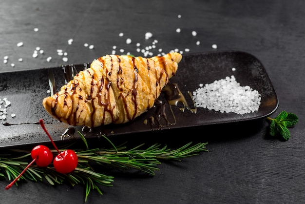 Leckeres Croissant mit Schokolade auf schwarzem Holzgrund