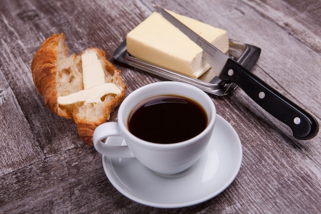 Leckeres Croissant neben einer Tasse Kaffee und Butter. Süßes Frühstück.
