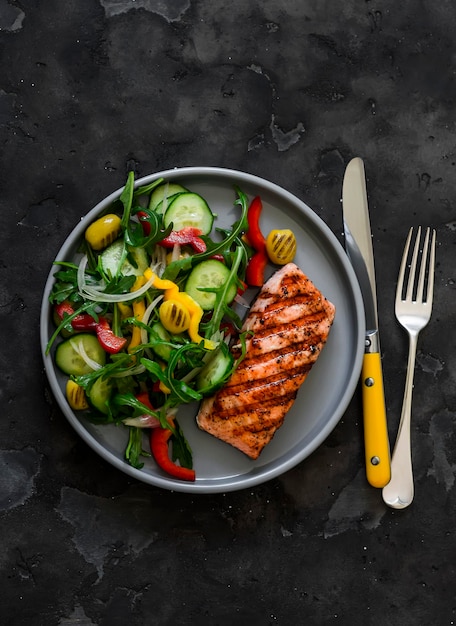 Leckeres Diät-Mittagessen, Grilllachs und frischer Gemüsesalat auf dunklem Hintergrund