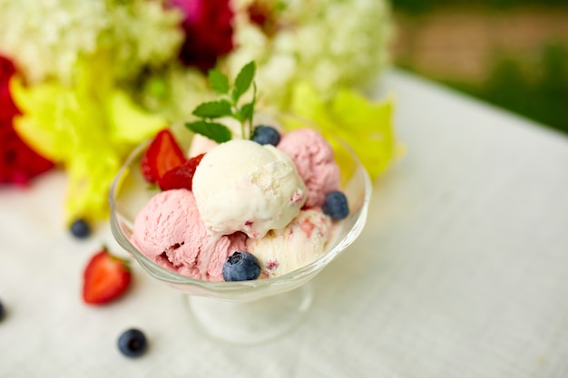 Leckeres Eis und frische Blaubeeren, Erdbeere in der Schüssel, präsentiert mit Blume auf einem Tisch in einem Garten während der Sommersaison für eine Party