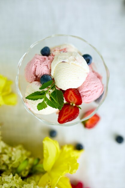 Leckeres Eis und frische Blaubeeren, Erdbeere in der Schüssel, präsentiert mit Blume auf einem Tisch in einem Garten während der Sommersaison für eine Party