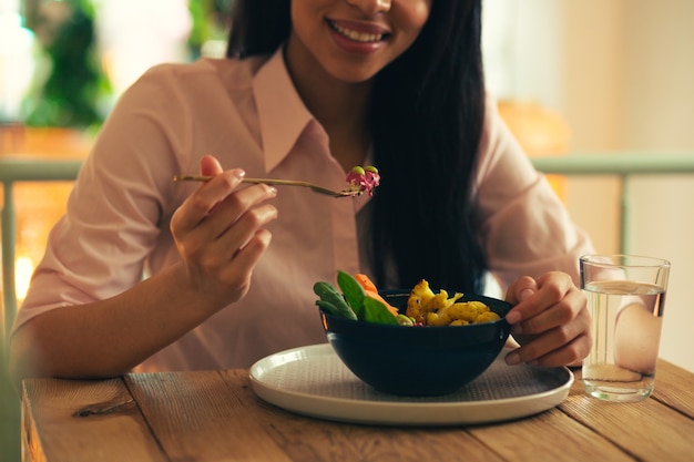 Leckeres Essen in einer Schüssel und junge lächelnde Dame, die es mit einer Gabel isst