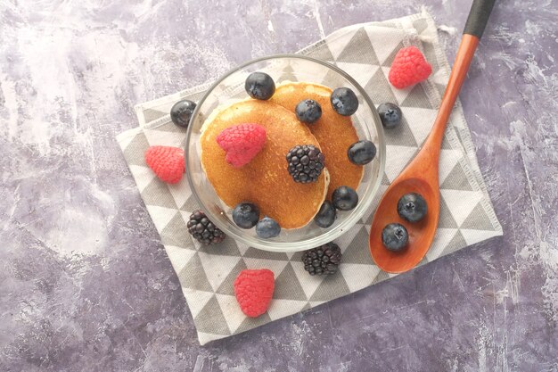 Leckeres Essen mit Beeren und Pfannenkuchen in einer Schüssel auf schwarzer Oberfläche