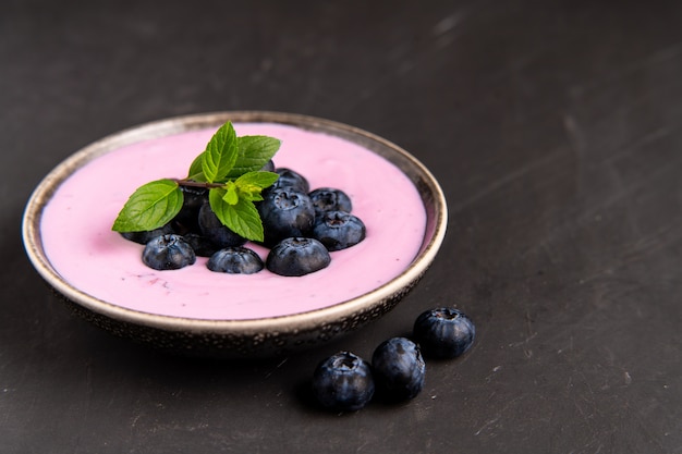 Leckeres frisches Blaubeerjoghurt-Schütteldessert in der Keramikschale, die auf schwarzem Tisch steht