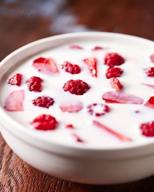 Leckeres frisches Essen mit weißer Milch und roten Himbeeren, Erdbeeren in einer weißen Schüssel auf Holzhintergrund.