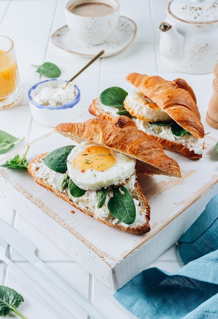 Leckeres Frühstück mit Croissant-Sandwiches mit Spiegelei, Spinat und Kaffee und Orangensaft