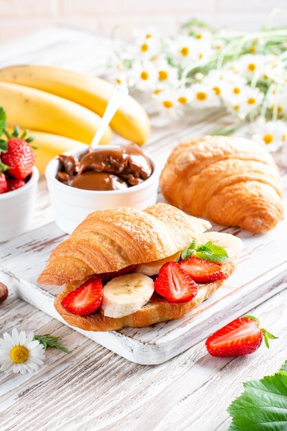 Leckeres frühstück mit frischen croissants, schokolade, banane und erdbeere auf holztisch. französisches gebäck