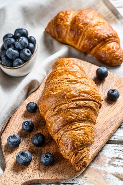 Leckeres Frühstück mit frischen Croissants und Blaubeeren. Weißer hölzerner Hintergrund. Draufsicht