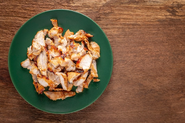 Leckeres, gebratenes Schweinefleisch in grüner Keramikplatte auf natürlichem Holzstrukturhintergrund mit Kopienraum für Text, Draufsicht