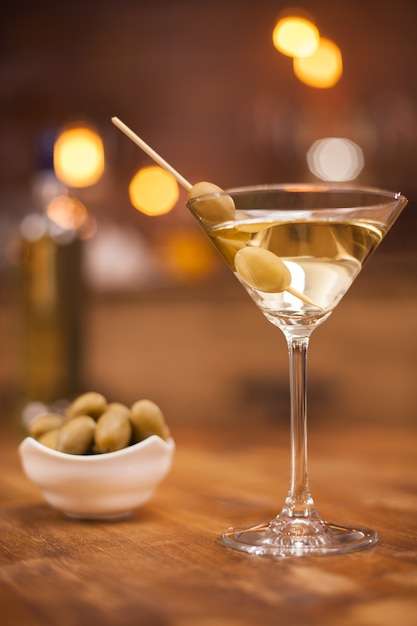 Leckeres Glas trockener Martini mit Oliven am Stiel und daneben eine Schüssel Oliven. Entspannen bei einem Glas Martini.