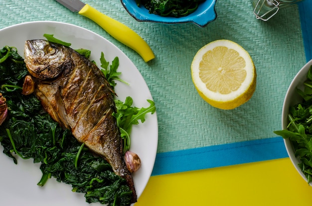 Leckeres italienisches Abendessen oder Mittagessen mit gebackenen Dorada-Fischen oder Seebrassen, garniert mit Spinat auf blauem Hintergrund