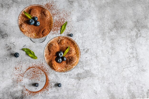 Leckeres italienisches Tiramisu in einer Glasschale mit Minze und Blaubeeren mit Copyspace auf Grau