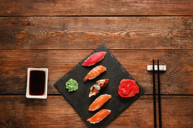 Leckeres köstliches Set aus fünf Sushi-Nigiri, serviert auf schwarzem Schiefer mit Ingwer und Wasabi, auf rustikalem Holztisch, flach. Japanische Küche, dunkler Hintergrund mit freiem Speicherplatz.