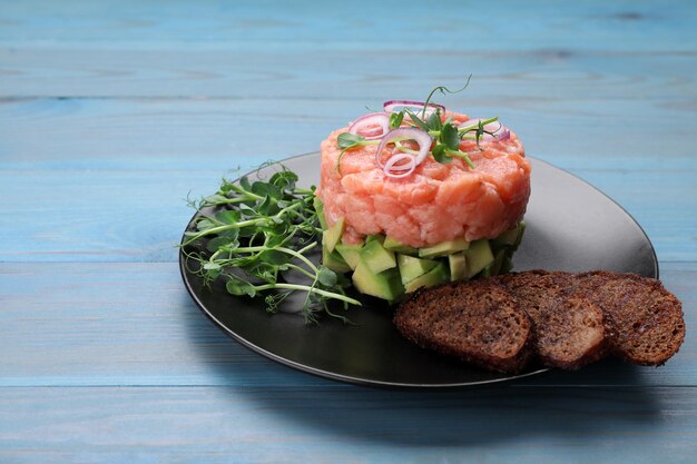 Foto leckeres lachstatar mit avocado-microgreens und croutons auf hellblauem holztisch. platz für text