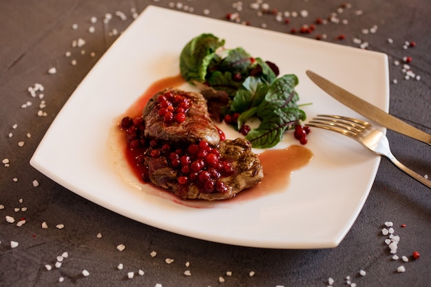 Leckeres Rindersteak mit Preiselbeeren und Rübenoberteilen auf dem weißen Teller.