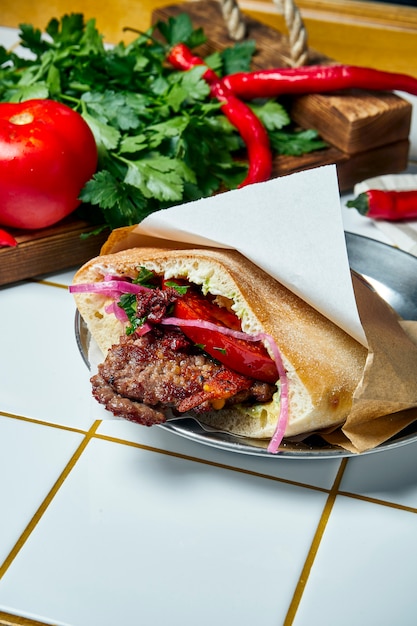 Leckeres Street Food - Pita mit Tomate, Zwiebel und Sauce, Beef Burger auf einem weißen Tisch. Griechische Küche. Aussicht.