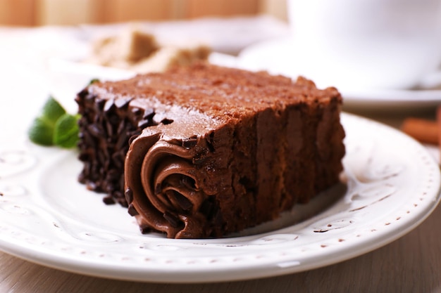 Leckeres Stück Schokoladenkuchen mit Minze und Zimt auf Holztisch und unscharfem Plankenhintergrund