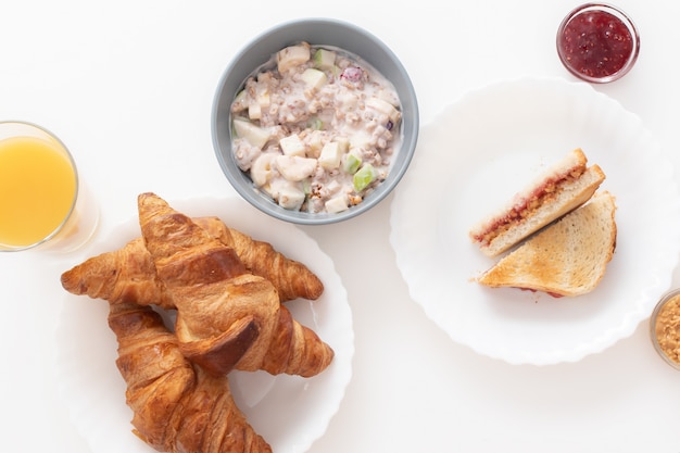 Leckeres und gesundes Frühstück. Croissants, Orangensaft, ein Sandwich mit Marmelade und Erdnussbutter, Müsli mit Joghurt, Banane und Apfel