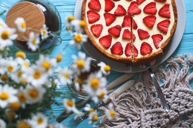 Leckeres und schönes Frühstück. Käsekuchen mit Erdbeeren auf einem hölzernen Hintergrund mit einem Strauß Gänseblümchen