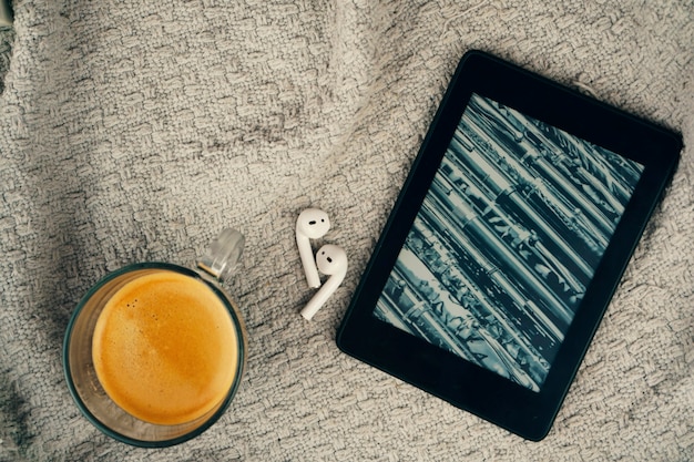 Lector de libros electrónicos, una taza de café y un auricular.