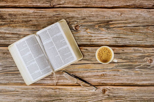 Lectura bíblica abierta de la mañana sobre una mesa con una taza de café y anteojos