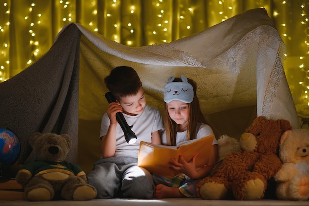 Lectura y juegos familiares en carpa infantil niño y niña con libro y linterna antes de acostarse