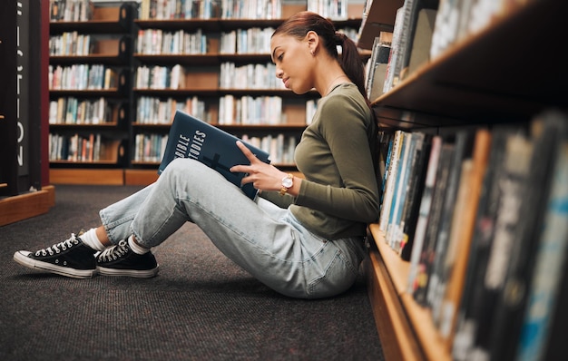 Lectura de libros y estudiante de biblioteca en el piso con aprendizaje, educación e investigación para la universidad escolar o la universidad con inspiración Historia de estudio de la Biblia de estantería y una mujer en el suelo leyendo un libro