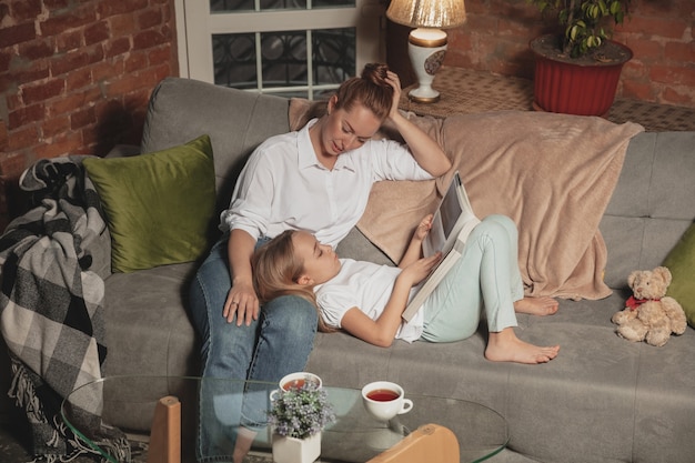 Lectura de libros. Madre e hija durante el autoaislamiento en casa mientras están en cuarentena, tiempo familiar acogedor y confortable, vida doméstica. Modelos sonrientes alegres y felices. Seguridad, prevención, concepto de amor.