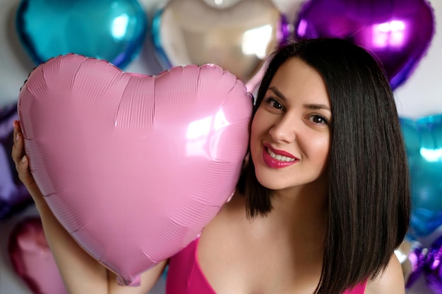 Ledy segura um balão rosa em forma de coração na mão, sorrindo docemente.