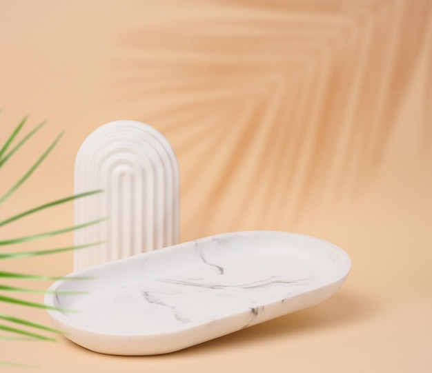 Leer ovaler weißer Marmor steht auf einem beigefarbenen Hintergrund und ein Schatten von Palmenlässen ist ein Ort, an dem Kosmetika und Produkte ausgestellt werden