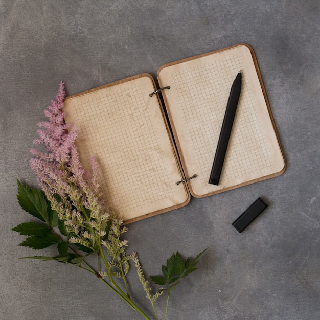 Leere Anmerkungsbuch der Draufsichtebene mit rosa Blumen, mehrfarbiger Astilba, Modell auf einem grauen Hintergrund. Textraum. Jahrgang. Hochzeits- oder Geburtstagseinladung oder Nachrichtenkonzept