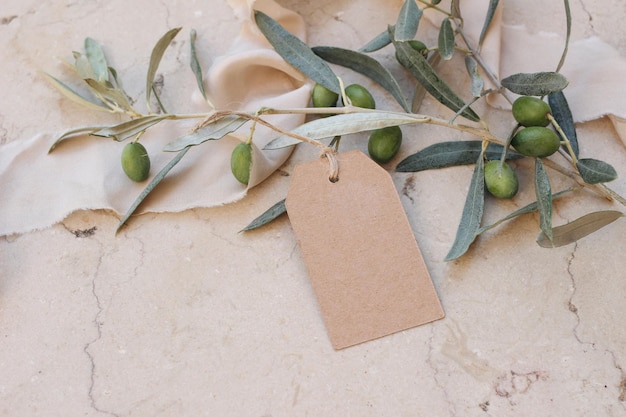 Leere Bastelpapier-Geschenkanhänger-Etikettenmodelle mit Olivenblättern und Ästen Seidenband-Marmor-Hintergrund Moderne Vorlage für Branding-Identität Sommerverkaufs-Geburtstags- oder Hochzeitskonzept Ansicht von oben