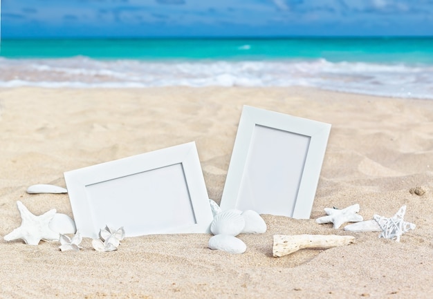 Leere Bilderrahmen auf dem Sandstrand mit Muscheln, Seesternen und Kerze.