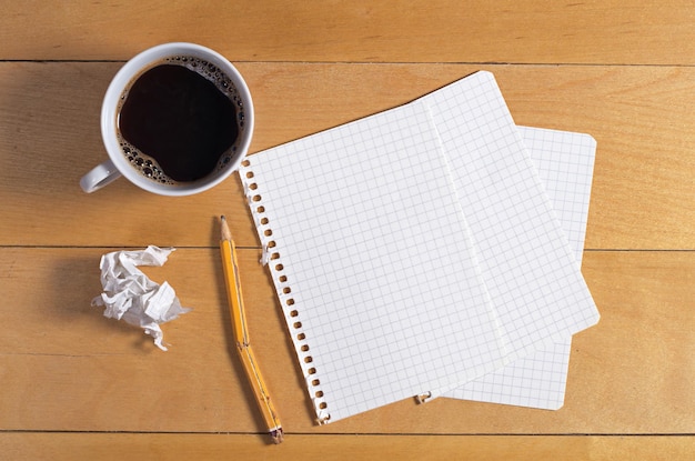 Leere Blätter Papier aus einem Notizbuch gebrochener Bleistift und zerknittertes Papier auf einem Holzschreibtisch mit Draufsicht einer Tasse Kaffee