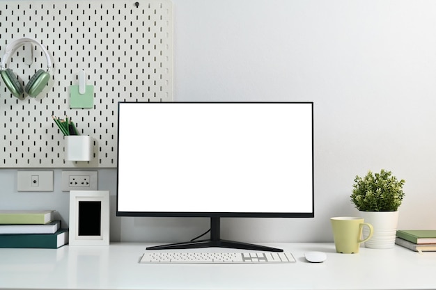 Leere Computermonitor, Kaffeekuppe, Hauspflanze und Schreibwaren auf weißem Tisch mit Pfahlbrett an der Wand