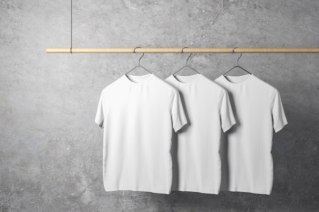 Leere drei weiße T-Shirts auf einem Kleiderbügel. Betonwandhintergrund. Designgeschäft und Stilkonzept. 3D-Rendering-Attrappe