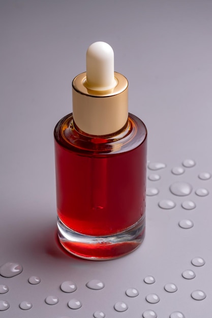 Leere Glasflasche mit ätherischem Öl mit Pipette auf grauem Hintergrund, dekorierte Wassertropfen, Hautpflege-Konzept mit natürlicher Kosmetik