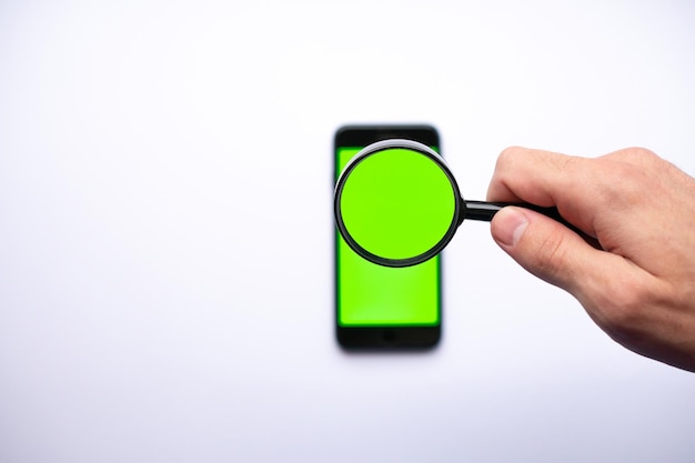 Leere Greenscreen-Vorlage für Smartphones mit Lupe in der Hand Such- und Explorationskonzept