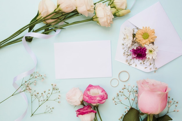 Leere hochzeitskarte mit zwei ringen und blumendekoration auf blauem hintergrund